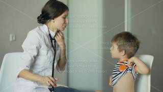 Young woman doctor talking little boy and listening with stethoscope in medical office