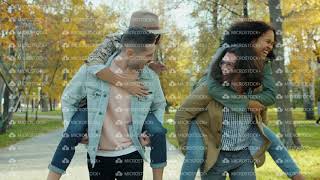 Joyful young men giving piggyback ride to happy women having fun in park