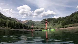 Side view of 2 paddle boarders moving across lake in the mountains